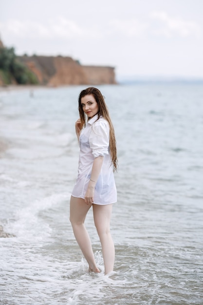 Mujer en ropa blanca refrescante a la orilla del mar.