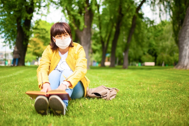 Mujer en ropa casual y máscara médica sentada en el parque