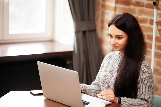 Mujer en ropa casual usando laptop y sonriendo mientras trabaja en interiores.