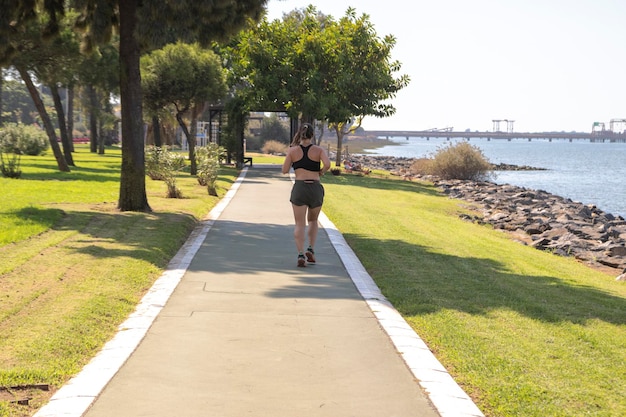 Mujer con ropa deportiva, corriendo por la orilla del río. Vista desde atrás. Ajuste el concepto de mujer.