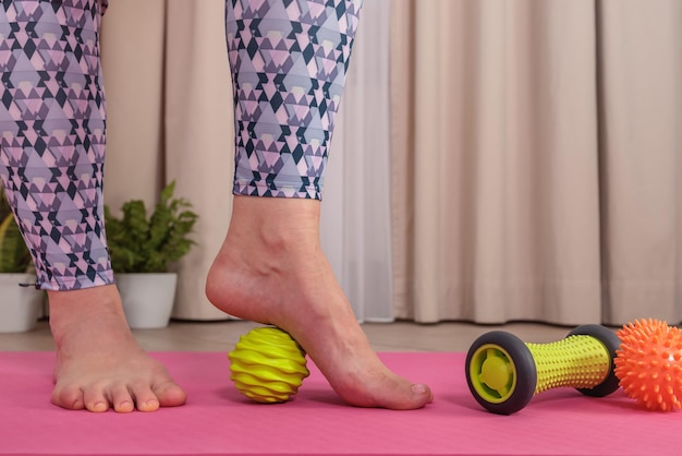 Una mujer con ropa deportiva de Veri Perry en una colchoneta de yoga rosa hace un masaje miofascial de pies en casa