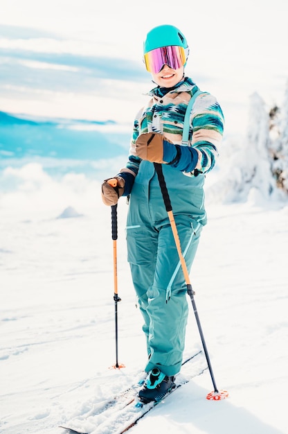 Mujer con ropa de esquí con casco y gafas de esquí en la cabeza con bastones de esquí Clima invernal en las pistas En la cima de una montaña y disfrutando de la vista Esquiador alpino Deporte de invierno