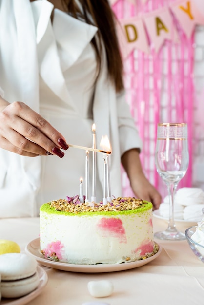 Mujer en ropa de fiesta blanca preparando la mesa de cumpleaños encendiendo las velas