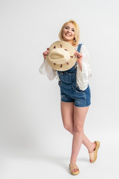 Mujer con ropa informal rústica con un sombrero en la mano posando sobre un fondo blanco