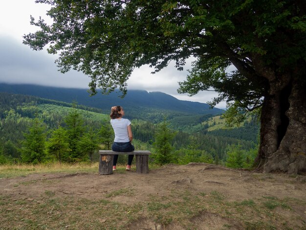 La mujer con ropa informal se sienta bajo un gran árbol con fondo forestal