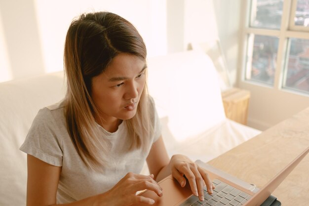 Mujer con ropa informal trabajando y escribiendo con su computadora portátil en su apartamento en concepto de