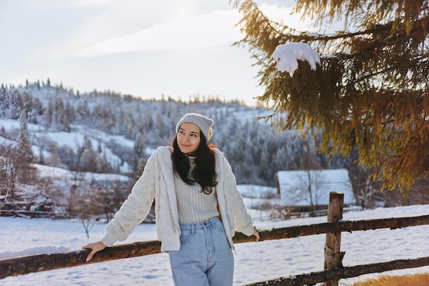 Mujer en ropa de invierno al aire libre contra montañas nevadas y aldea