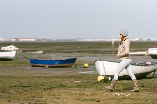 Mujer con ropa de invierno cruza una zona de barcos de pesca durante la marea baja