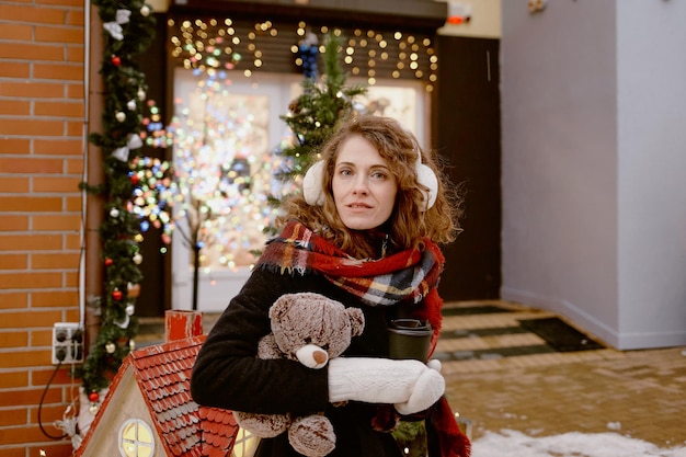 Foto mujer con ropa de invierno y orejeras de piel con oso de peluche en el mercado navideño. chica al aire libre