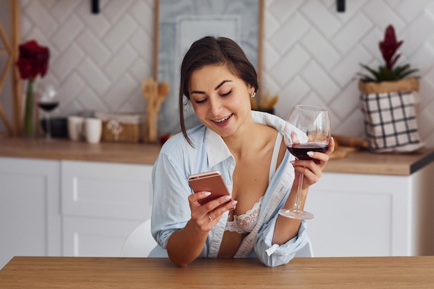 Mujer en ropa ligera está en la cocina con copa de vino.