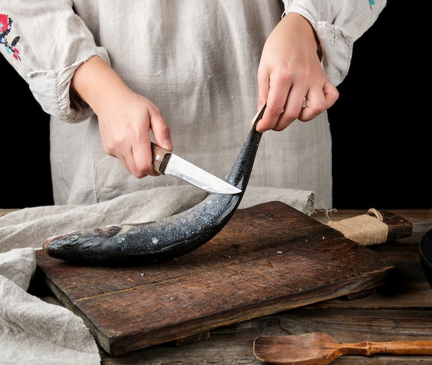 Mujer en ropa de lino gris limpia la lubina de pescado