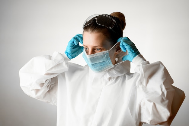 Mujer en ropa protectora y guantes de látex poniéndose una máscara en la cara