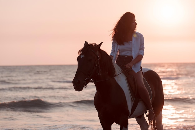 Mujer con ropa de verano disfruta montando a caballo en una hermosa playa de arena al atardecer enfoque selectivo