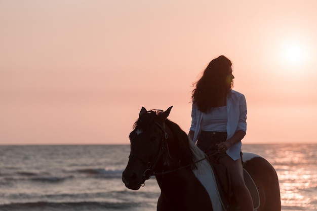 Mujer con ropa de verano disfruta montando a caballo en una hermosa playa de arena al atardecer enfoque selectivo