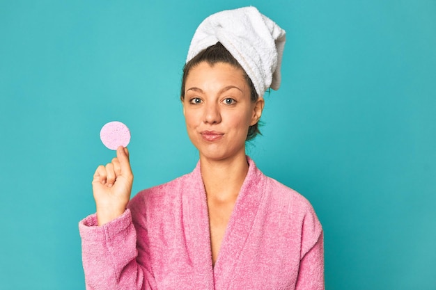 Mujer de rostro fresco con esponja de maquillaje sonriendo con túnica rosa