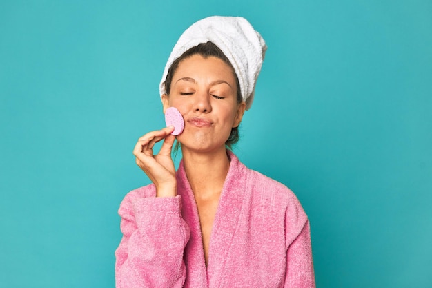 Mujer de rostro fresco con esponja de maquillaje sonriendo con túnica rosa