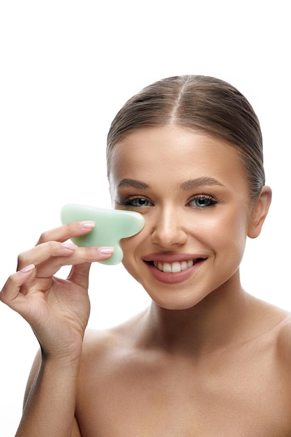 Mujer con rostro hermoso usando gua sha facial Hermosa chica sonriente haciendo masaje facial SpaSkin care