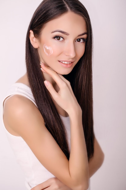 Mujer con rostro sano aplicando crema cosmética debajo de los ojos