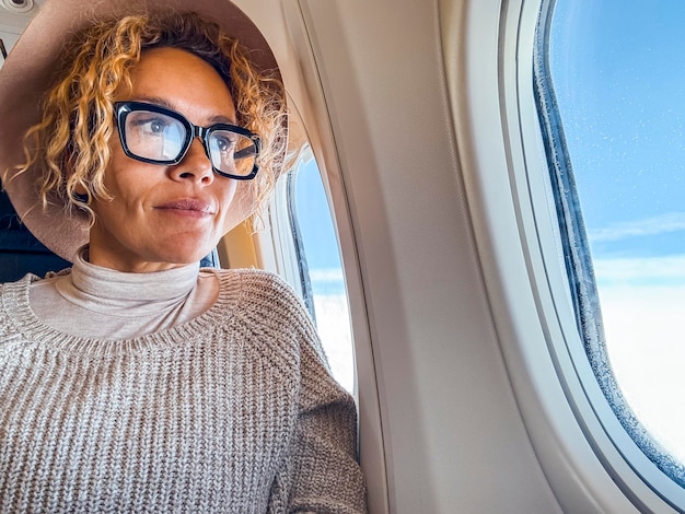 Mujer rubia de 45 años con gafas sentada en un asiento de avión mirando por la ventana está sonriendo y disfrutando del tiempo durante un viaje de vacaciones concepto de viaje