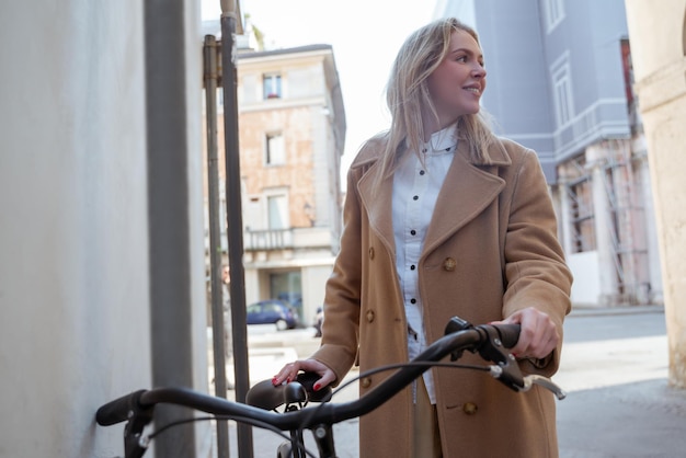 Mujer rubia con un abrigo beige con una bicicleta en la calle