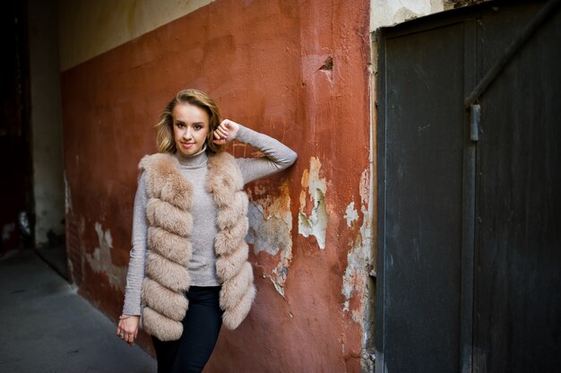 La mujer rubia en el abrigo de pieles presentó contra la pared anaranjada vieja.