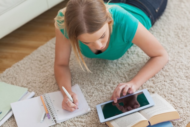 Mujer rubia acostada en el piso usando tableta para hacer su tarea