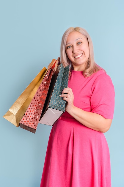 Una mujer rubia adulta de 40 años sostiene muchas bolsas de compras en sus manos sobre una foto vertical de fondo azul