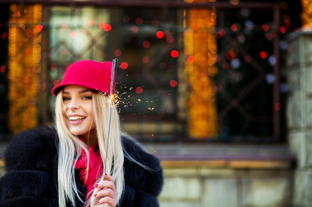 Mujer rubia alegre celebrando el año nuevo con luces de Bengala en el fondo bokeh. Espacio para texto