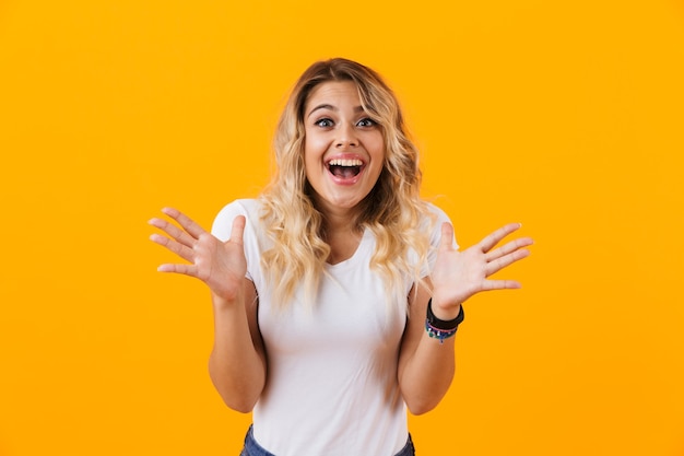 Mujer rubia alegre en ropa básica preguntándose y sonriendo, aislado sobre pared amarilla