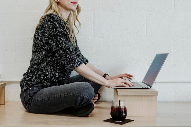 Mujer rubia alegre usando una computadora portátil en un piso de madera