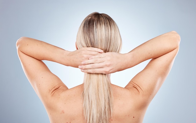 Mujer rubia y atar el cabello en la espalda en el estudio para cosméticos de belleza y bienestar contra el fondo azul Modelar el cuidado del cabello y la salud para el brillo cosmético cuidado personal natural y saludable por telón de fondo