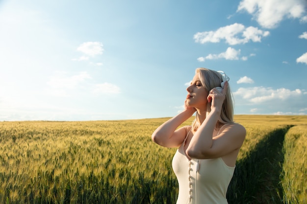 Mujer rubia en auriculares bailando en campo de trigo en verano