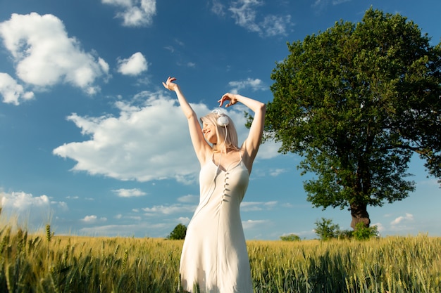 Mujer rubia en auriculares bailando en campo de trigo en verano