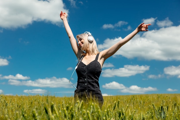 Mujer rubia con auriculares en campo de trigo en día soleado