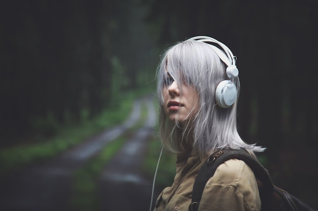 Mujer rubia en auriculares con mochila en día lluvioso en bosque