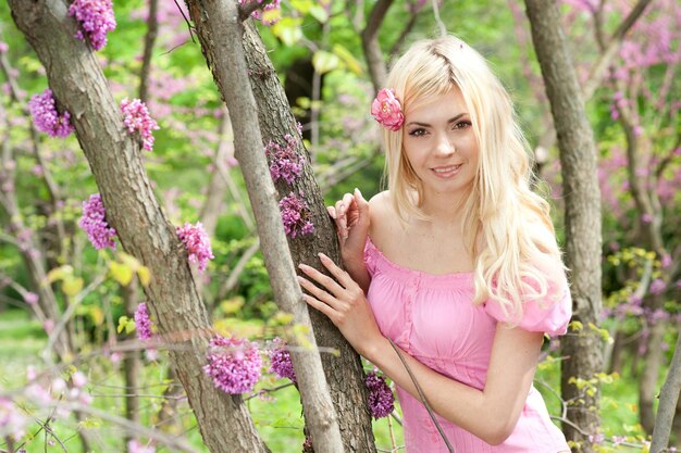 Mujer rubia bastante feliz posando en el parque floreciente de primavera