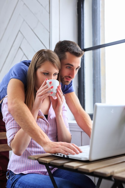 Mujer rubia bebiendo café y un hombre trabaja con una laptop.