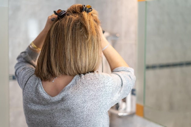 Mujer rubia blanca con cabello lacio después de arreglarlo con un dispositivo de planchado eléctrico