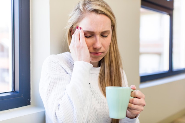 Mujer rubia bonita adulta joven que sostiene una taza de café en casa