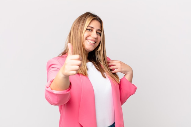 Mujer rubia bonita con curvas que se siente orgullosa, sonriendo positivamente con los pulgares hacia arriba