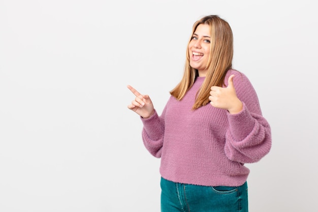 Mujer rubia bonita con curvas que se siente orgullosa sonriendo positivamente con los pulgares hacia arriba