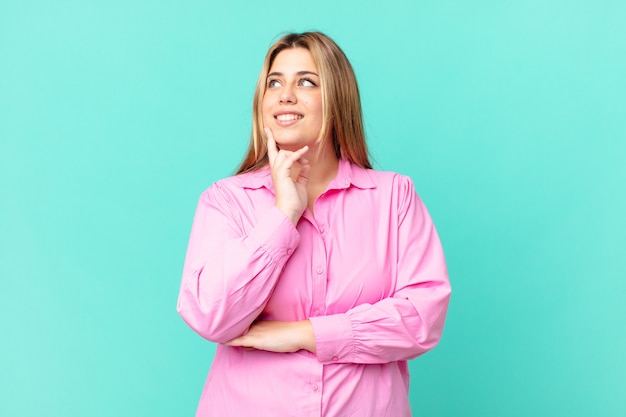 Mujer rubia bonita con curvas sonriendo felizmente y soñando despierto o dudando