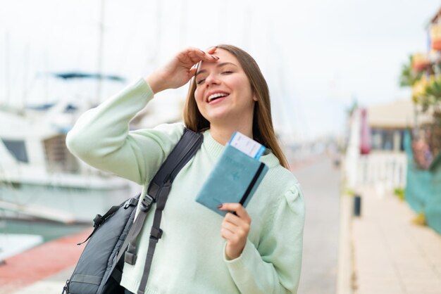 Mujer rubia bonita joven que sostiene un pasaporte con expresión sorprendida