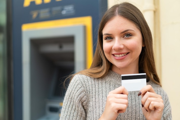 Mujer rubia bonita joven que usa un cajero automático