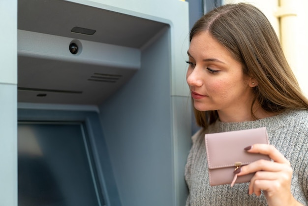 Mujer rubia bonita joven que usa un cajero automático