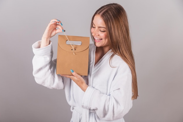 Mujer rubia brasileña que muestra un cabello maravilloso vestido con una túnica sosteniendo una bolsa de cartón con cosméticos y un primer plano del cabello