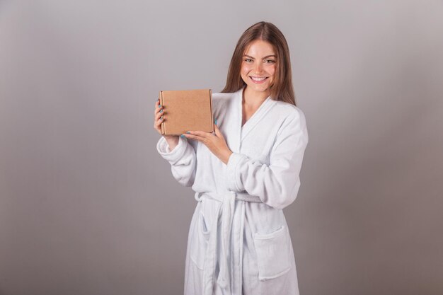 Mujer rubia brasileña que muestra un cabello maravilloso vestido con una túnica sosteniendo pequeñas cajas de cartón con cosméticos