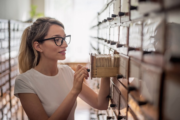 Mujer rubia buscando archivos de libros en catálogo viejo