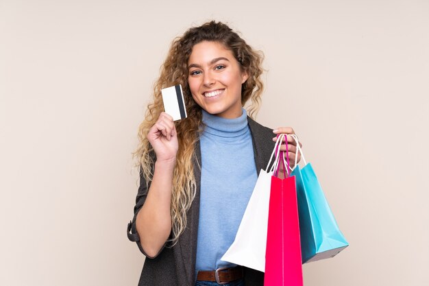 Mujer rubia con cabello rizado aislado sosteniendo bolsas de compras y una tarjeta de crédito