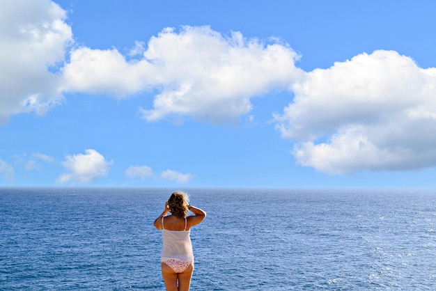 Mujer rubia de cabello rizado en bikini tomando una foto con el móvil en la playa en el horizonte